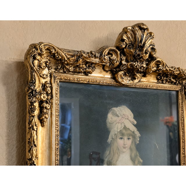Elegant vintage gilt wall mirror featuring ornate detailing and a charming portrait accent at the top. Its tall, narrow...