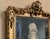 Elegant vintage gilt wall mirror featuring ornate detailing and a charming portrait accent at the top. Its tall, narrow...