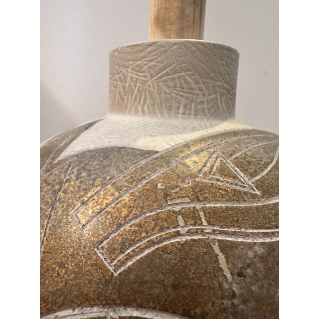 A vintage ceramic lamp base featuring intricate geometric carvings and a warm metallic‑bronze glaze contrasted with a...