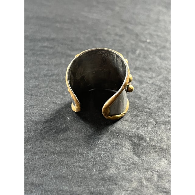 Vintage mixed metal ring with a wide band and sculptural raised detailing in brass and copper over a silver-tone base. The...