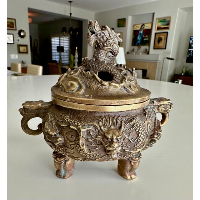 Well crafted Chinese brass or bronze incense burner with three legs, stylized dragon handles, and a finial lid sculpted as...