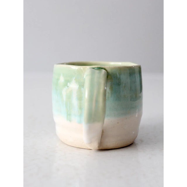 This is a vintage studio pottery mug. Signed by the artist, the handmade mug has a pretty pastel green and blue drip glaze...