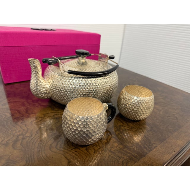 Design Plus Gallery presents a Hammered Steel Tea Set with Fuchsia Gift Box. The surface of the kettle and cups is...