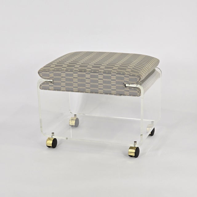 Post-Modern lucite ottoman or vanity seat with waterfall sides, a lower shelf, and gold-tone casters for versatility. Made...