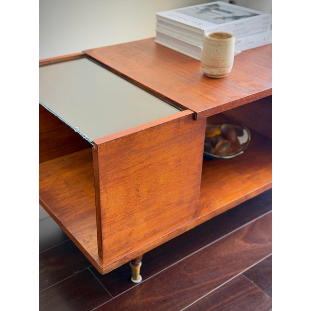 A MCM architectural 1960s mid-century modern coffee table crafted in warm teak veneer and wood. The raised central wood...