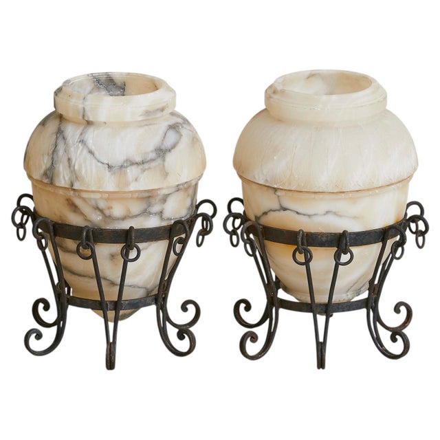 A French alabaster vase from the 20th century, cradled in a hand-forged wrought-iron stand. The vessel is carved from...