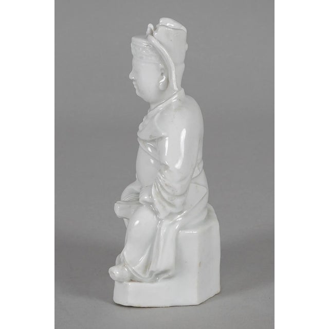 Chinese small white porcelain figure of a seated official wearing robes and elaborate headdress.