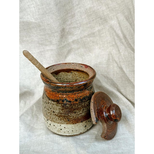 This small handcrafted stoneware pot, complete with its original carved lid and wooden spoon, is a tribute to functional...