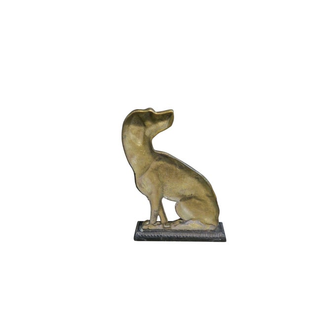 A seated dog looking backward. The dog is brass and base is iron.