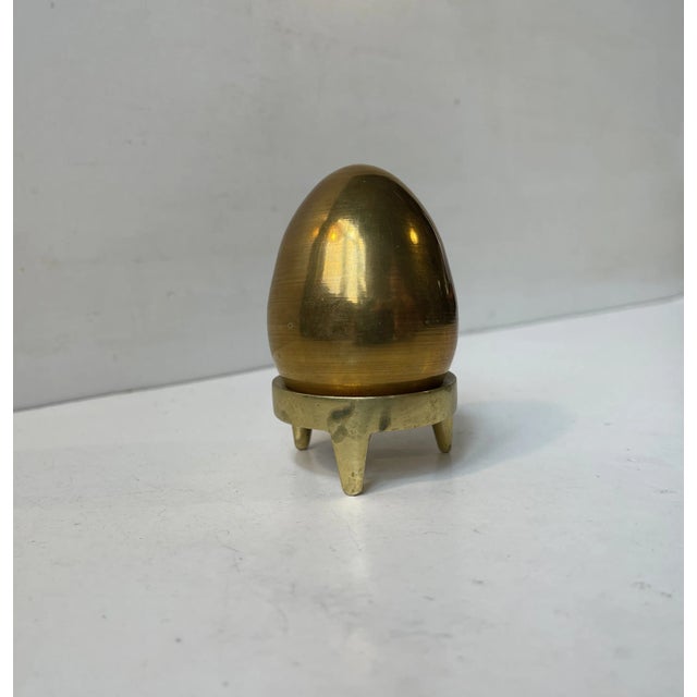 A bronze egg displayed on a brass stand. Designed and made by Illums Bolighus in Copenhagen, Denmark circa 1960. The egg...