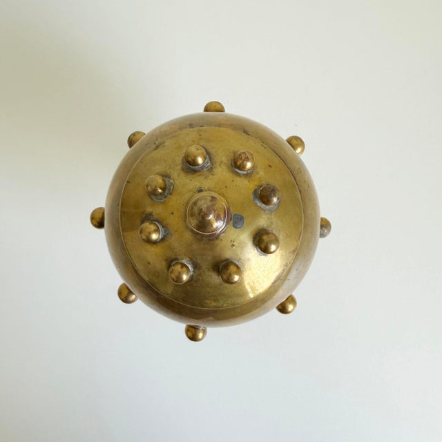 Unique sculptural brass box featuring an orb-shaped lidded compartment, adorned with brass studs, atop a pedestal base....