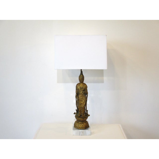 A Mid Century gold gilt metal Buddha table lamp with Lucite base and topped with an off white linen shade in the style of...