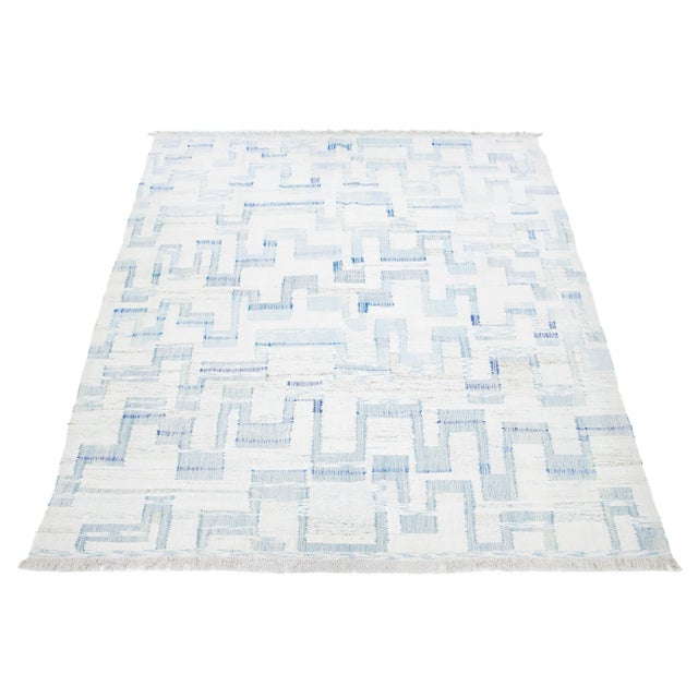 This rug features a modern Kilim flatweave design made from wool, with an ivory base and an abstract blue motif. This rug...