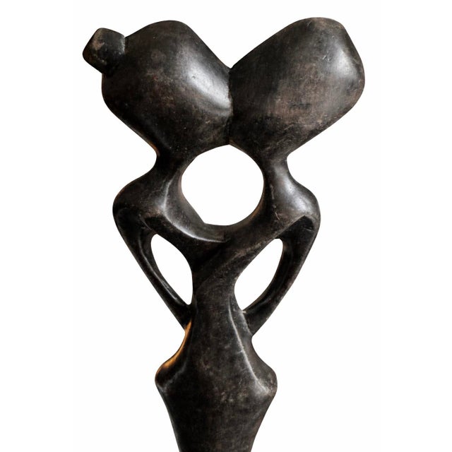 Hand-carved wood sculpture depicting an abstract couple in a unified, flowing form. The elongated figures and negative...