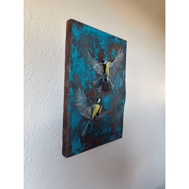 The artwork depicts two birds in mid-flight, their wings outstretched against a vibrant blue background that contrasts...