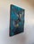 The artwork depicts two birds in mid-flight, their wings outstretched against a vibrant blue background that contrasts...