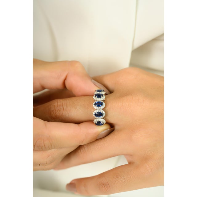 A captivating blend of elegance and color, this 14K white gold band ring showcases five vibrant oval-cut sapphires with a...
