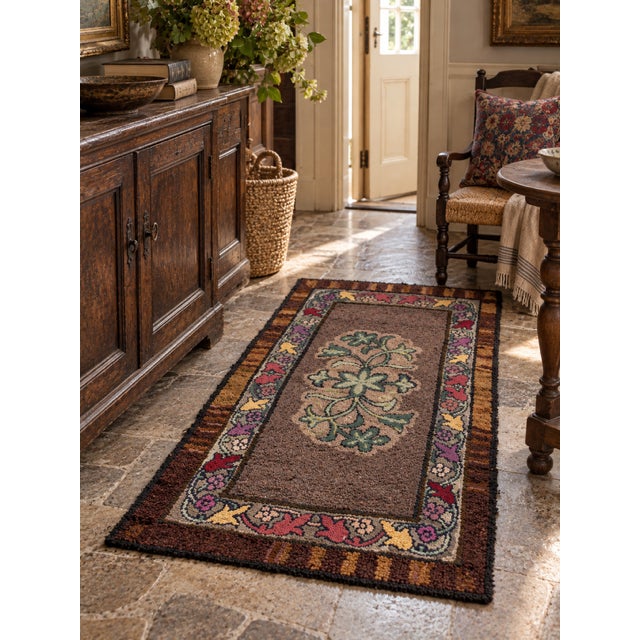 An antique hand-hooked rug featuring a stylized green floral motif against a muted brown field, framed by a colorful...