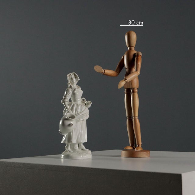 White porcelain figurine depicting a female figure with a jar and basket. Ginori trademark under the base. This piece is...