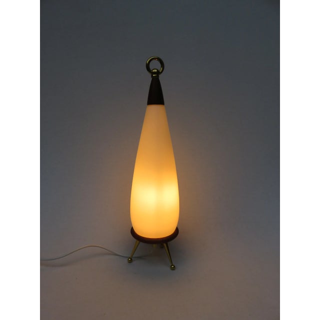 This lamp is made of teak, a brass tripod, and a brass ring. The lampshade is made of frosted glass. The lamp has an E27...