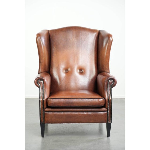 This sheepskin wingback chair is crafted in a warm cognac color and features a refined finish with decorative studs. The...