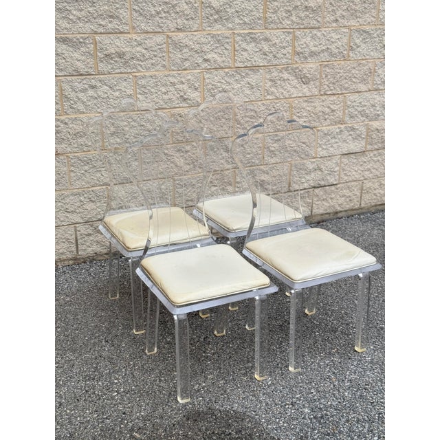 Mid-Century Modern set of four Lucite dining chairs from the 1970s-1980s. The chairs feature clear acrylic frames with...