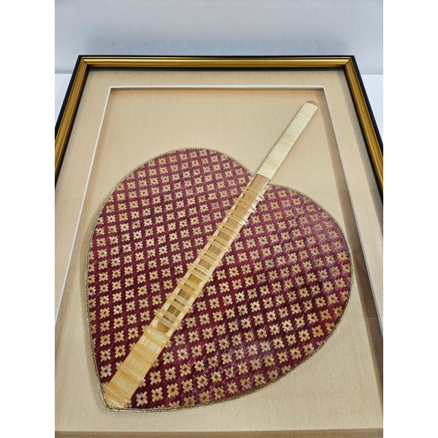 This red and tan woven rattan hand fan is from Thailand and is heart shaped. The fan is mounted in a golden silk fabric in...