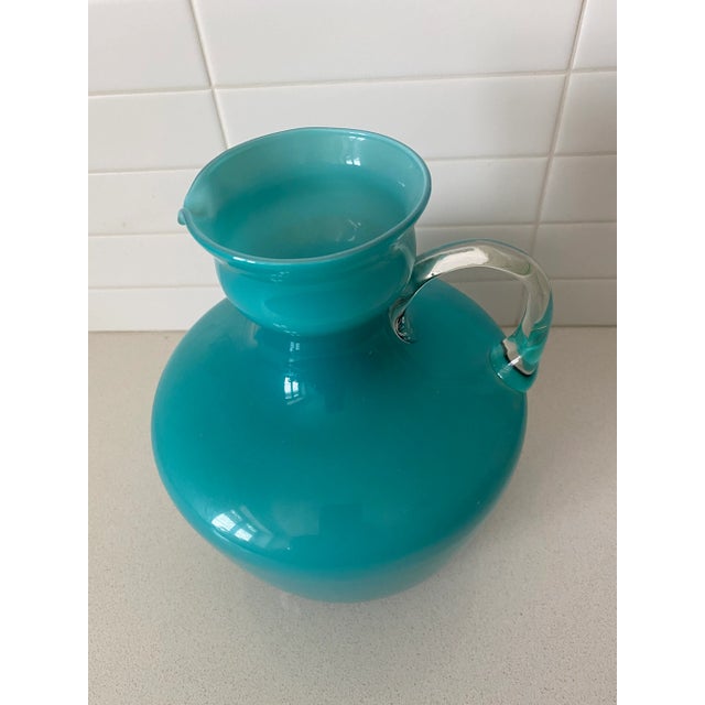Add a splash of color to your room with this lovely hand-blown pitcher featuring a turquoise cased glass body with a clear...