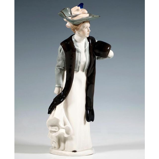 Elegant lady wearing a wide-brimmed hat decorated with a pink ribbon and blue feather, a floor-length white gown, a light...