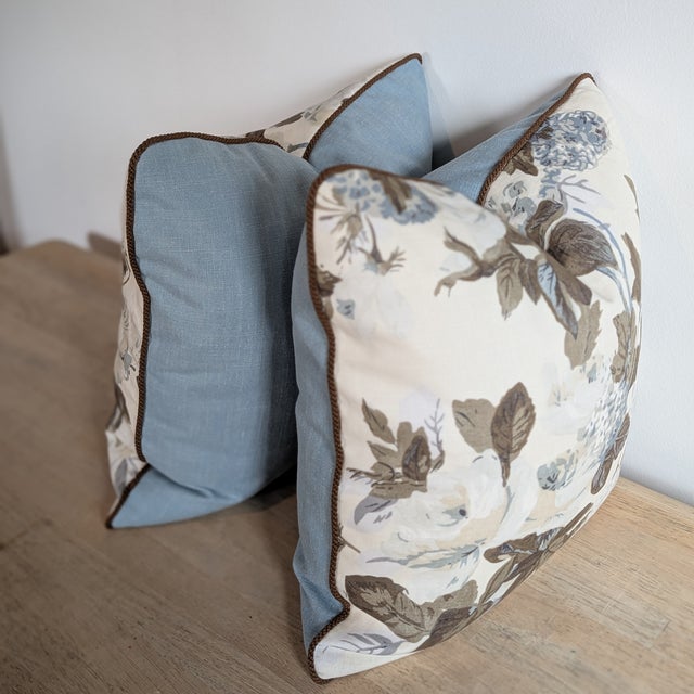 Cowtan & Tout Rose and Hydrangea pillows in platinum teak, with coordinating brown braided cord and blue linen backs....