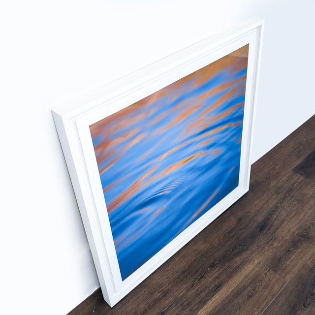 This is a modern framed print featuring abstract water ripples in vivid blue and orange tones. The print comes in a sturdy...