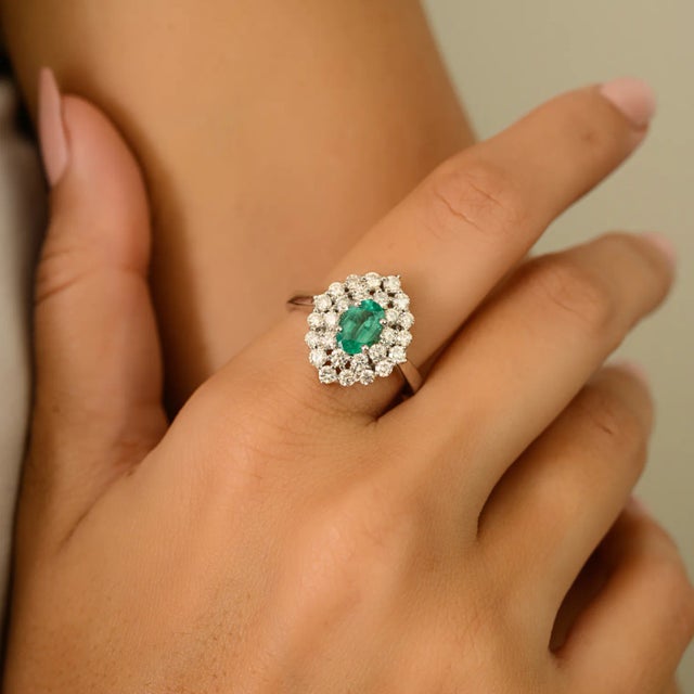This vintage-inspired oval 0.79-carat natural emerald in the center and 0.94 carats of round halo brilliant-cut diamond...