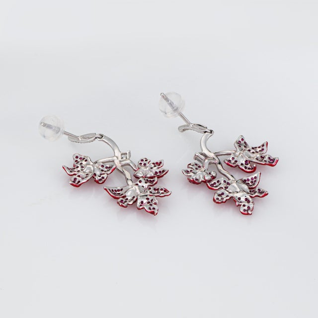 Stylish contemporary ruby & diamond maple leaf drop earrings crafted in 18k white gold. Diamonds total an estimated 0.50...