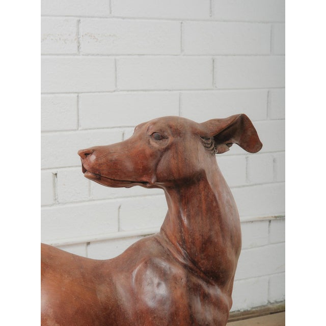 A striking hand-carved wooden sculpture depicting a sleek greyhound in motion, captured mid-stride with elegant, elongated...