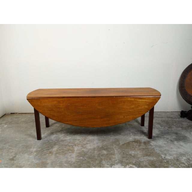 An English walnut drop leaf table from the 19th century, with oval top and straight legs. Created in England during the...