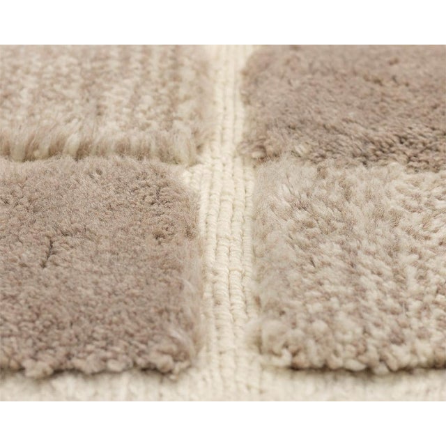 Elegant hand-knotted wool rug displaying a checkerboard design in complementary earthy Beige tones, delivering a classic...