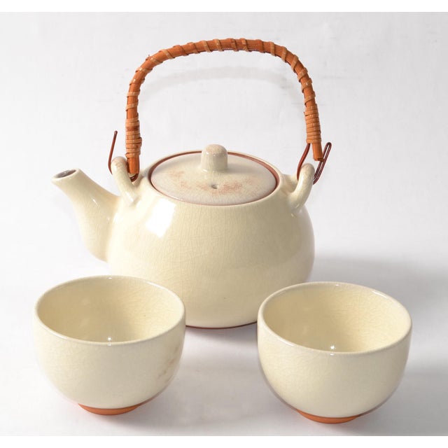 This vintage Kotobuki tea set includes one top-handled teapot and two teacups each featuring a beige glaze and brown...