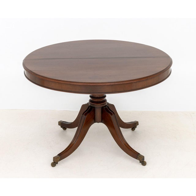 Regency Style Mahogany Pedestal Dining Table, the circular top above four fluted legs terminating in casters. 29.5" H x...