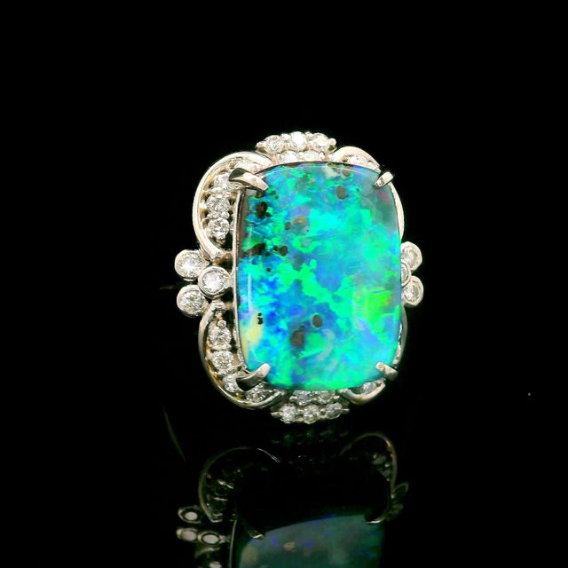 A captivating opal takes center stage, its cushion shape revealing a mesmerizing rainbow of colors. Surrounding the opal,...