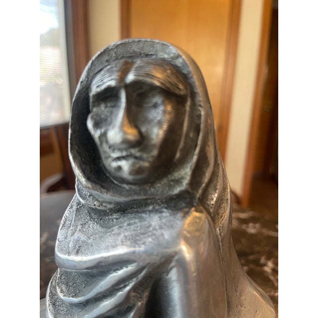 Pewter Sculpture of Seated Woman in Her Wrap. Marking. Sculpture sits on a wood base, 2 inches tall.