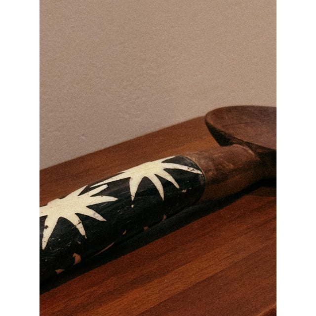 Large carved wooden decorative spoon with a handle embellished by geometric inlays, creating a striking visual contrast...