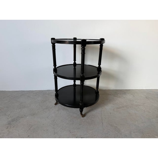 Elegant 1960s Hollywood Regency three-tier side table featuring a sophisticated black ebonized finish, turned spindle...