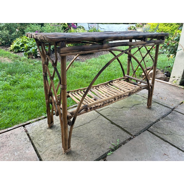 Handcrafted rustic twig console table featuring a slatted top, decorative bentwood arches, lattice sides, and a lower...