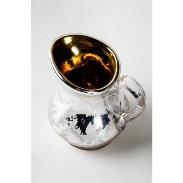 Pitcher enameled with bird and wreath. Mercury Glass with gold interior. Applied glass handle. Size: 5.25"W x 4.25"D x 5.25"H