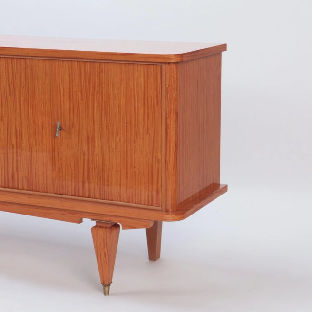 A Mid Century Modern French two door sideboard with exotic satinwood veneers and spade feet ending in brass sabots. C 1960.