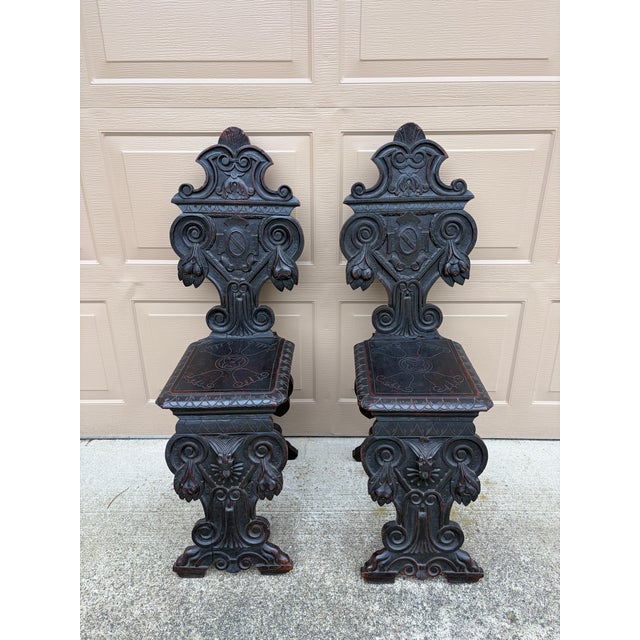 A striking pair of antique Italian Renaissance Revival hall chairs crafted from richly toned walnut and adorned with...