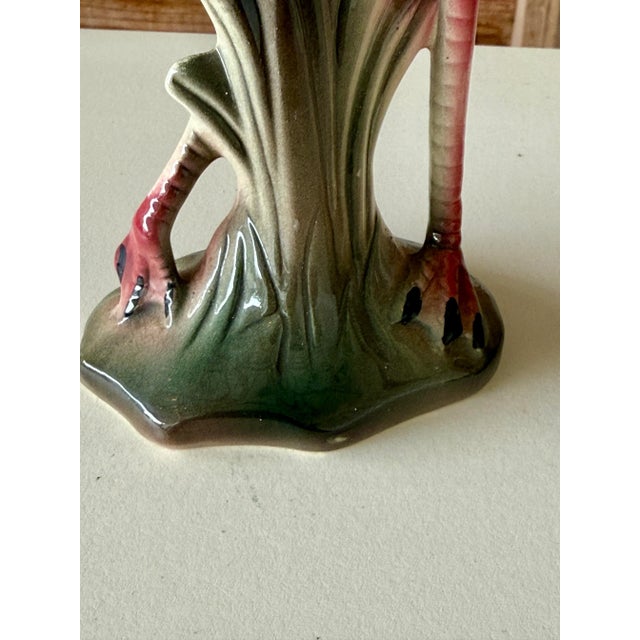 A charming pair of mid-20th century ceramic flamingo figurines featuring vibrant pink and green glazed finishes with...