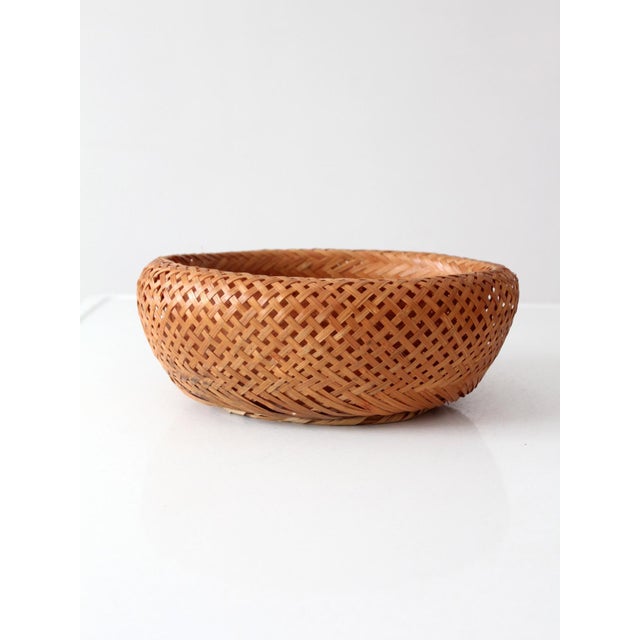 A vintage handwoven bamboo basket bowl featuring a rounded silhouette, gently curved rim, and intricate open lattice weave...