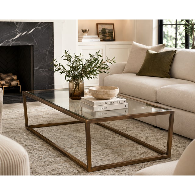 A handsome rectangular coffee table by Arhaus featuring a clean, architectural metal frame in a warm bronze finish with an...
