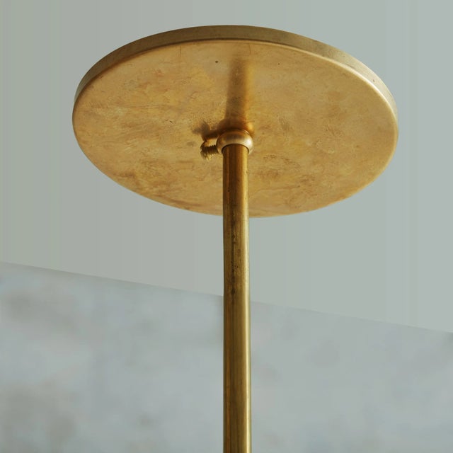 A vintage brass pendant light featuring a delicately tapered cylindrical brass shade with a perforated metal trim along...